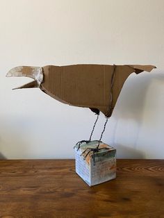 a bird made out of cardboard sitting on top of a wooden table next to a box