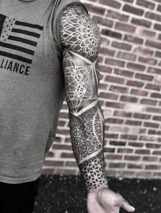 a man with a tattoo on his arm and arms is standing in front of a brick wall