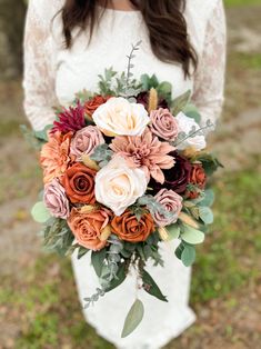 a woman holding a bouquet of flowers in her hands and wearing a white dress with lace sleeves