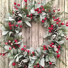 a wreath with holly, pine cones and red berries is hung on a wooden wall