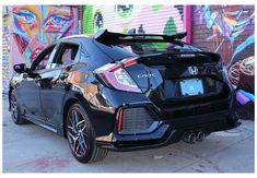 the rear end of a black honda civic hatchback parked in front of graffiti covered wall