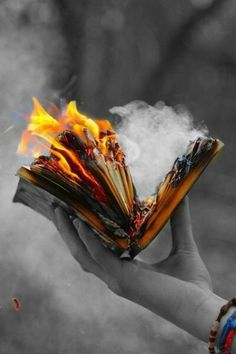 a person holding an open book in their hand with fire coming out of the pages