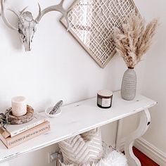 a white table topped with a vase filled with flowers next to a wall mounted deer head