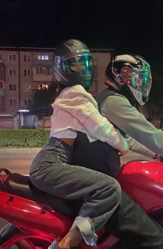 two people riding on the back of a red motorcycle at night with their helmets on