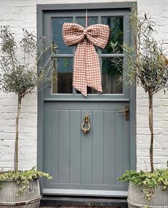 a bow on the front door of a white brick house with potted trees and two planters