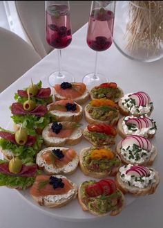 a white plate topped with lots of sandwiches and veggies next to wine glasses