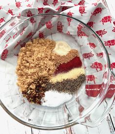 a glass bowl filled with different types of food on top of a wooden table next to a red and white towel