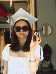 a woman taking a selfie with her graduation cap and gown on, in front of a mirror