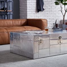 a silver trunk sitting on top of a floor next to a couch