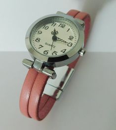 This is a tailor-made wristwatch for women. The watch is round, 1 inch diameter, made in alloy, free of nickel and lead, silver finish. The quadrant is silver tone, with numerals and three needles. The band will be made to fit your wrist. The band is made with European quality leather. The clasp could be magnetic or fold-over style. Comes with an extra battery and in a gift box. Adjustable Pink Analog Watches, Pink Analog Watches, Pink Adjustable Watch With Round Dial, Pink Adjustable Watch, Pink Analog Watch Accessories With Round Dial, Pink Analog Watch With Round Dial, Pink Watches With Adjustable Bracelet Strap, Pink Watches With Bracelet Strap And Adjustable Fit, Pastel Pink Color