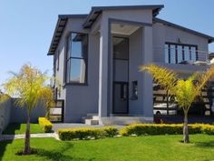 a house that is in the middle of some grass and trees with bushes around it