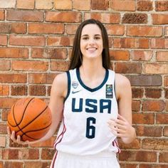 a woman holding a basketball standing in front of a brick wall with the usa number 6 on it