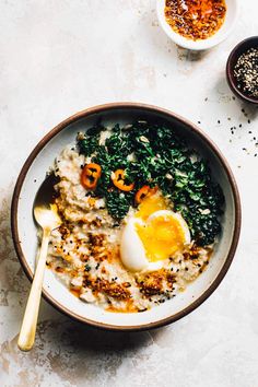 a bowl filled with oatmeal topped with an egg and spinach next to two bowls of seasoning