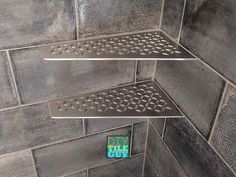 two metal shelves in the corner of a tiled shower stall, one with holes on it