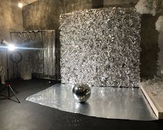 a silver ball sitting on top of a metal sheet in front of a light fixture