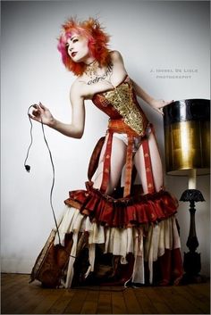 a woman with red hair wearing a costume and holding a drum in one hand while standing on a wooden floor