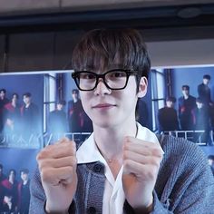 a young man wearing glasses standing in front of a poster with his hands up to the camera