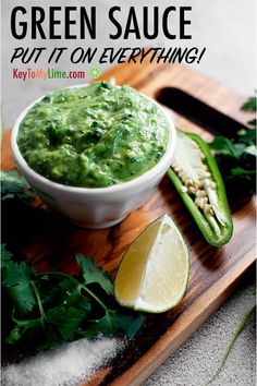 green sauce in a white bowl on a wooden cutting board with limes and cilantro