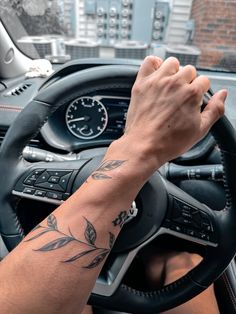 a person driving a car with their hand on the steering wheel and tattoos on his arm