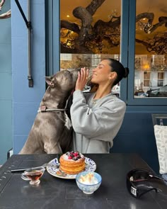 a woman sitting at a table with a dog and cake in front of her,