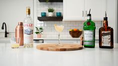 bottles and glasses on a kitchen counter with a cutting board in the foreground next to them