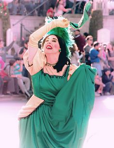 a woman in a green dress is dancing with her hands behind her head while people watch