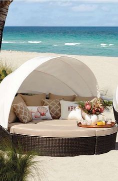 an outdoor day bed on the beach with pillows and flowers in vases next to it