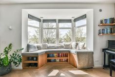 a living room filled with furniture and a piano in front of a large window next to a bookshelf