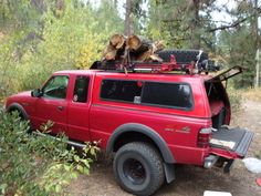 a red pick up truck parked in the woods with logs on it's roof