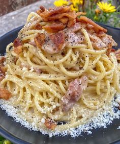 pasta with bacon and parmesan cheese on a plate next to some daisies