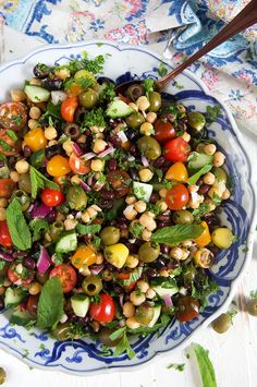 a salad with olives, tomatoes, cucumbers and green herbs in a blue and white bowl