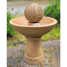 a stone fountain with two balls in it on the ground next to grass and bushes