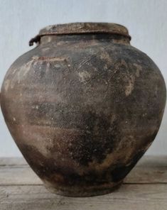 an old brown vase sitting on top of a wooden table next to a white wall