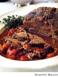 a white plate topped with meat and tomato sauce next to a bowl of soup on top of a table