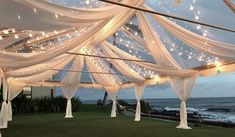 the inside of a wedding tent with white drapes and lights