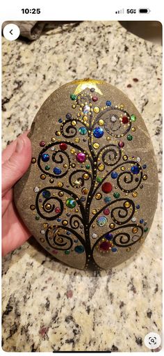 a hand holding a rock with a tree painted on it's side, in front of a marble counter top