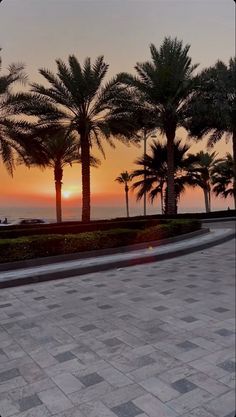 the sun is setting behind palm trees in front of an oceanfront walkway with people walking on it