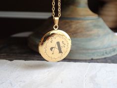 "Beautiful and classic, this round Victorian-inspired locket necklace features places for two photos inside. Personalize yours a vintage calligraphy initial with a floral motif surround. This treasured keepsake pendant and chain are both 14k gold plated stainless steel so are both hypo-allergenic and tarnish proof.   This locket isn't just a piece of jewelry; it's a vessel for your most precious memories. Whether it's a token of love, a symbol of a cherished bond, or a memento of a significant moment, this customizable gold locket holds the promise of preserving what matters most to you. Wear it close to your heart, carrying a photo, a tiny keepsake, or a secret message--whatever holds significance for you. Its versatile style seamlessly complements any outfit, making it a timeless additio Initial Pendant Locket Necklace For Anniversary, Locket Necklace For Mother's Day, Personalized Gold Locket Necklace For Birthday, Initials Locket Necklace For Anniversary, Personalized Round Locket Necklace For Wedding, Vintage Round Locket Necklace With Engraving Option, Vintage Round Locket Necklace For Anniversary, Initials Medallion Locket Necklace Keepsake, Initials Medallion Locket Necklace For Keepsake