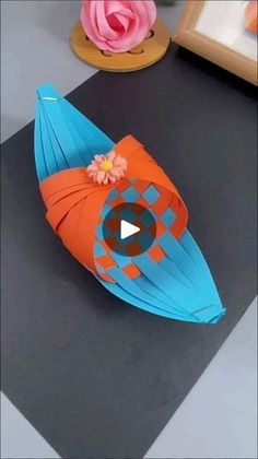 an orange and blue paper boat sitting on top of a black table next to pink flowers