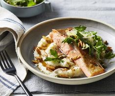 a white plate topped with fish and mashed potatoes next to a bowl of salad