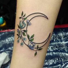 a tattoo on the leg of a woman with blue flowers and a crescent shaped moon