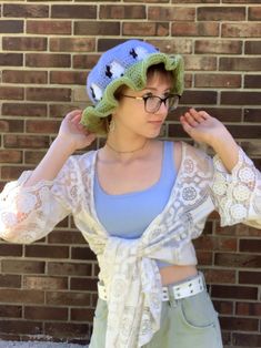 a woman with glasses and a knitted hat is standing in front of a brick wall