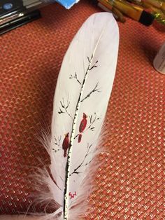 a white feather with red birds painted on it sitting next to some markers and pens