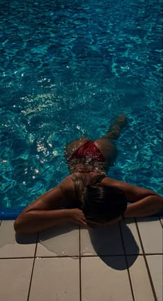 a woman laying on the ground in front of a swimming pool with her back to the camera