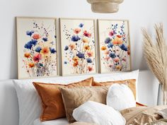 three paintings on the wall above a bed with white linens and pillows, along with some dried grass