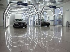 two cars are parked in an empty car showroom with lights on the ceiling above them