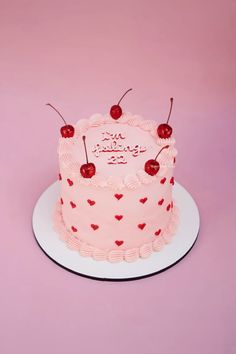 a pink birthday cake with cherries on top