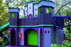 a purple and green play house in the middle of some trees with a slide next to it