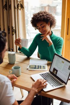 two people sitting at a table with laptops and coffee cups in front of them