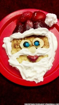 a red plate topped with pancakes covered in whipped cream and a face made out of strawberries